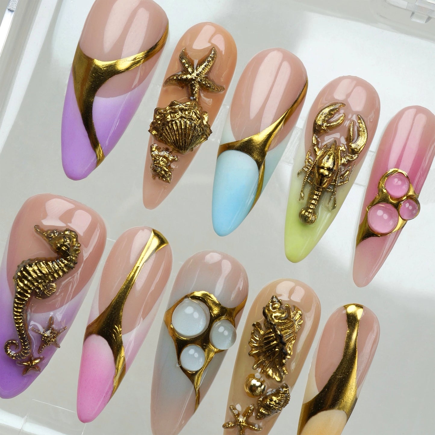 Press-on nails by Donailsart with gold under-the-sea elements on pastel ombré designs