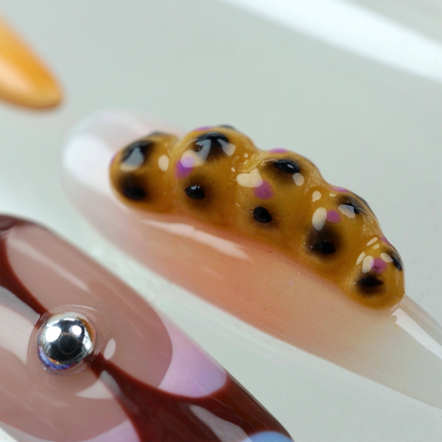Vibrant press-on nails from Donailsart showcasing 3D flowers, animal spots, fruit textures, and abstract patterns in purple, orange, and nude tones