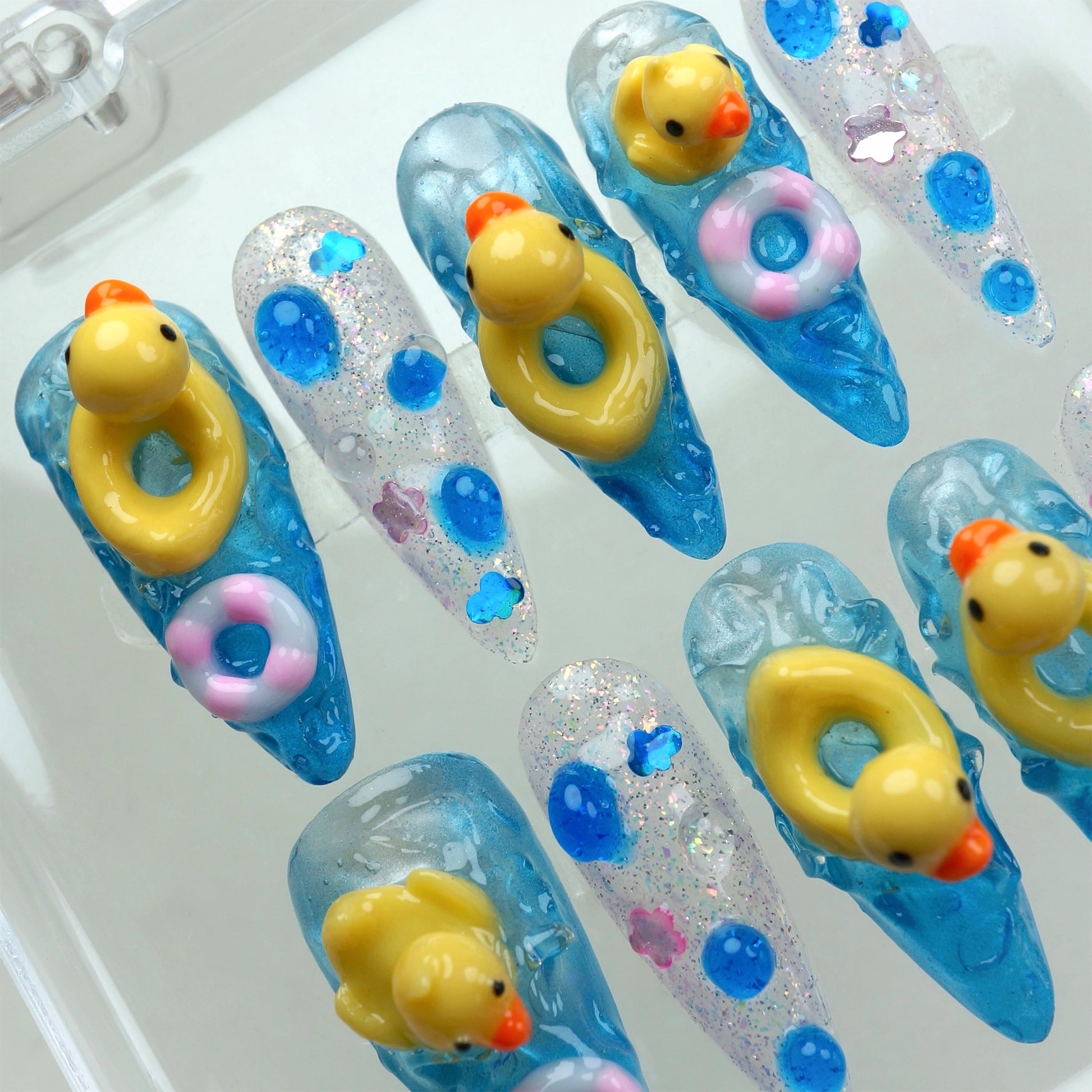 Funny nail design featuring 3D rubber ducks and colorful float rings on glittery blue water-effect nails