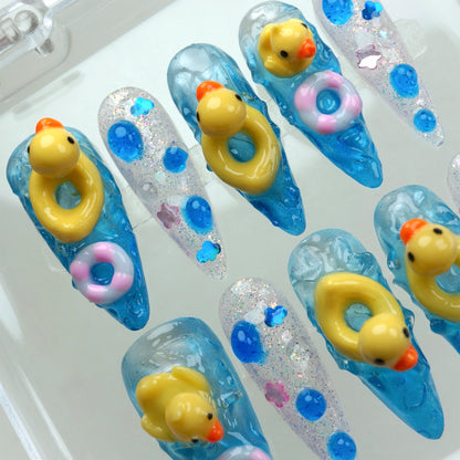 Funny nail design featuring 3D rubber ducks and colorful float rings on glittery blue water-effect nails