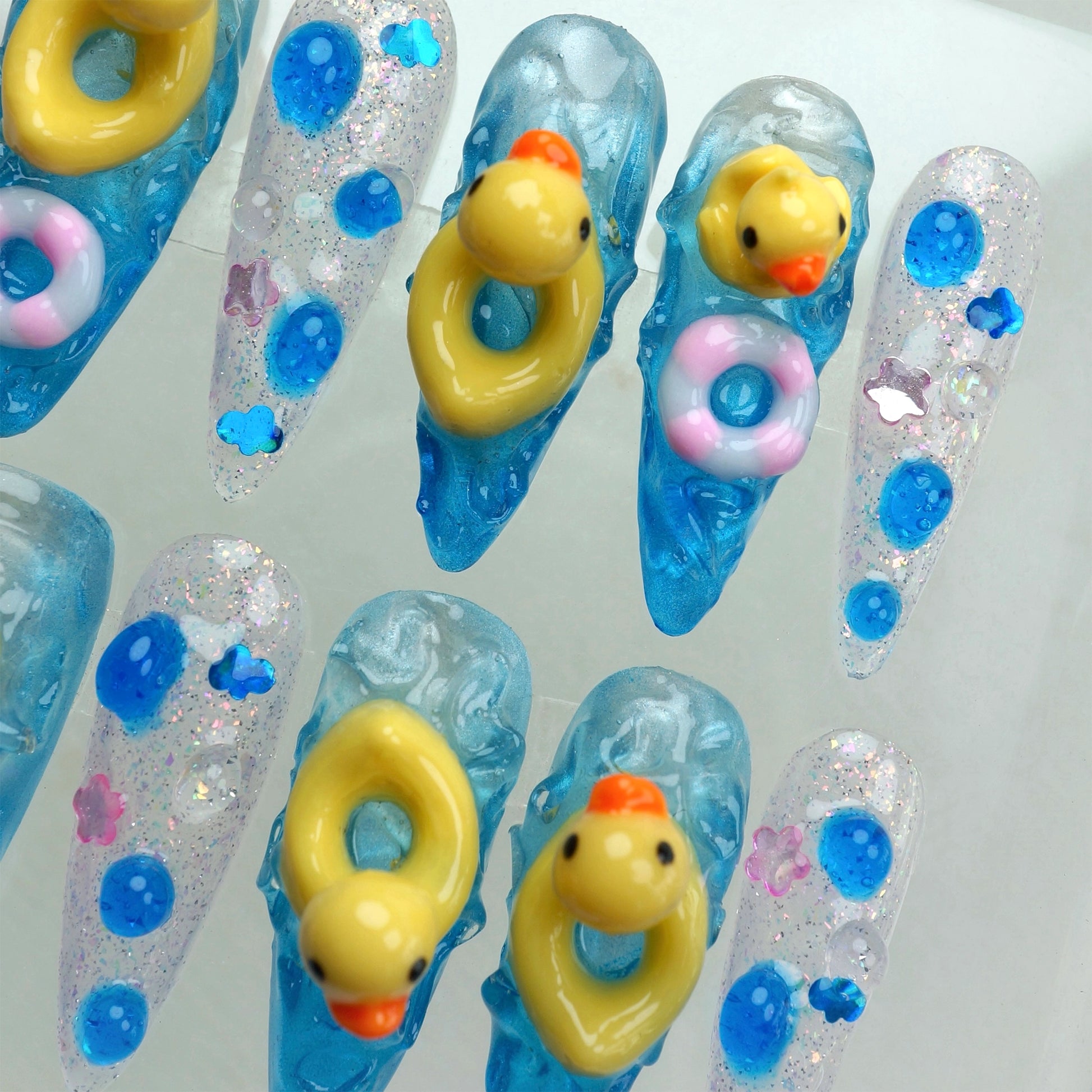 Playful funny nail art set with blue water textures, glitter accents, and tiny 3D duck figures