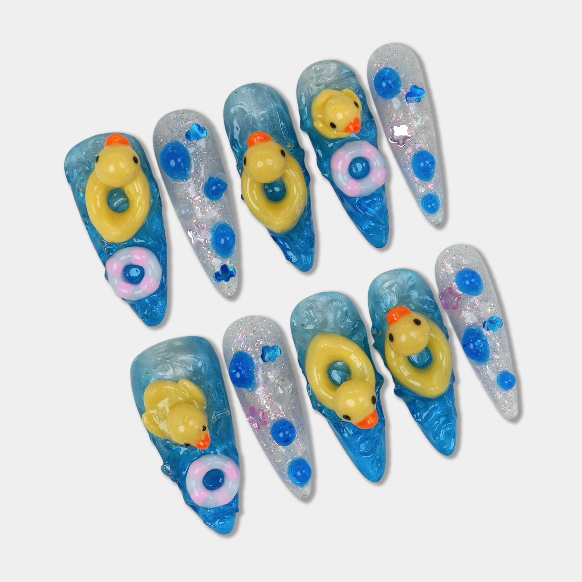 Funny nail design featuring 3D rubber ducks and colorful float rings on glittery blue water-effect nails
