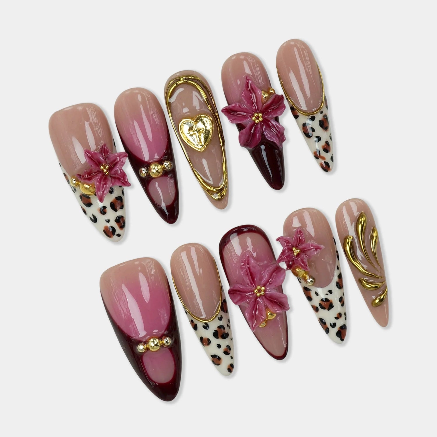 Floral Rouge press-on nail set flat lay showing almond nails: blush-to-wine ombre nails, white leopard print nails, dark burgundy wine glossy nails, 3D deep pink rose flower charms with gold stamen beads, gold oval frame with heart-cross charm, gold ball studs, and gold vine swirl art on pinky nail