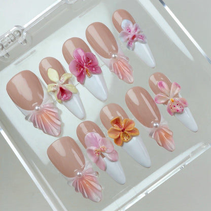 Set of flower nails featuring nude and white French tips, 3D orchids in pink, yellow, and orange, and pearl embellishments