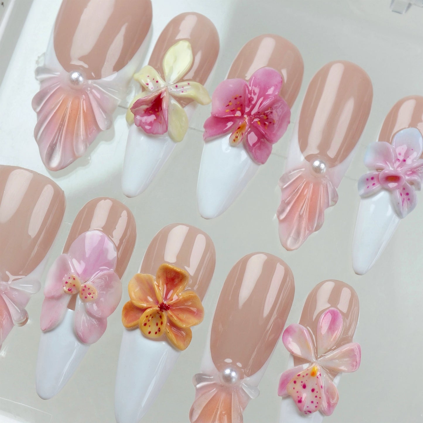 3D flower nails with nude and white base, detailed orchid designs, and pearl seashell accents for a soft floral look