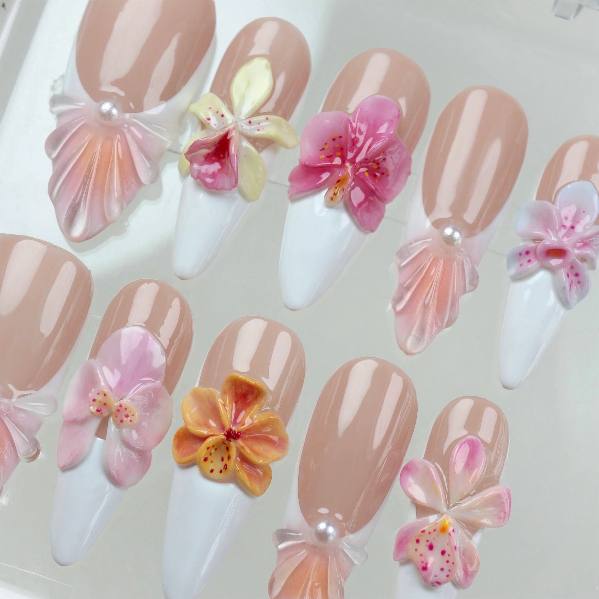 3D flower nails with nude and white base, detailed orchid designs, and pearl seashell accents for a soft floral look