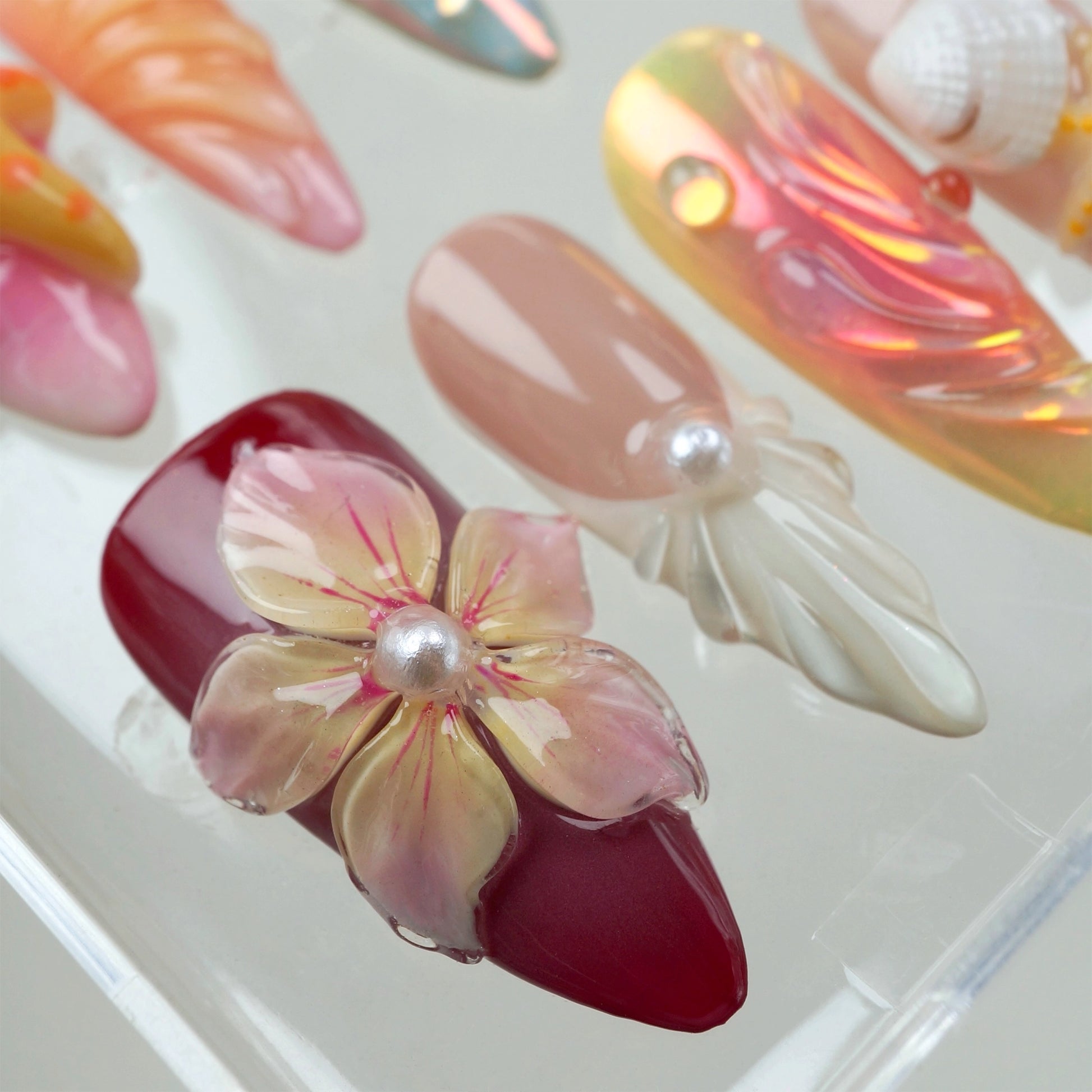 Handcrafted ocean-themed press-on nails with 3D starfish, seashells, and floral designs in pink and iridescent shades, displayed in a clear case