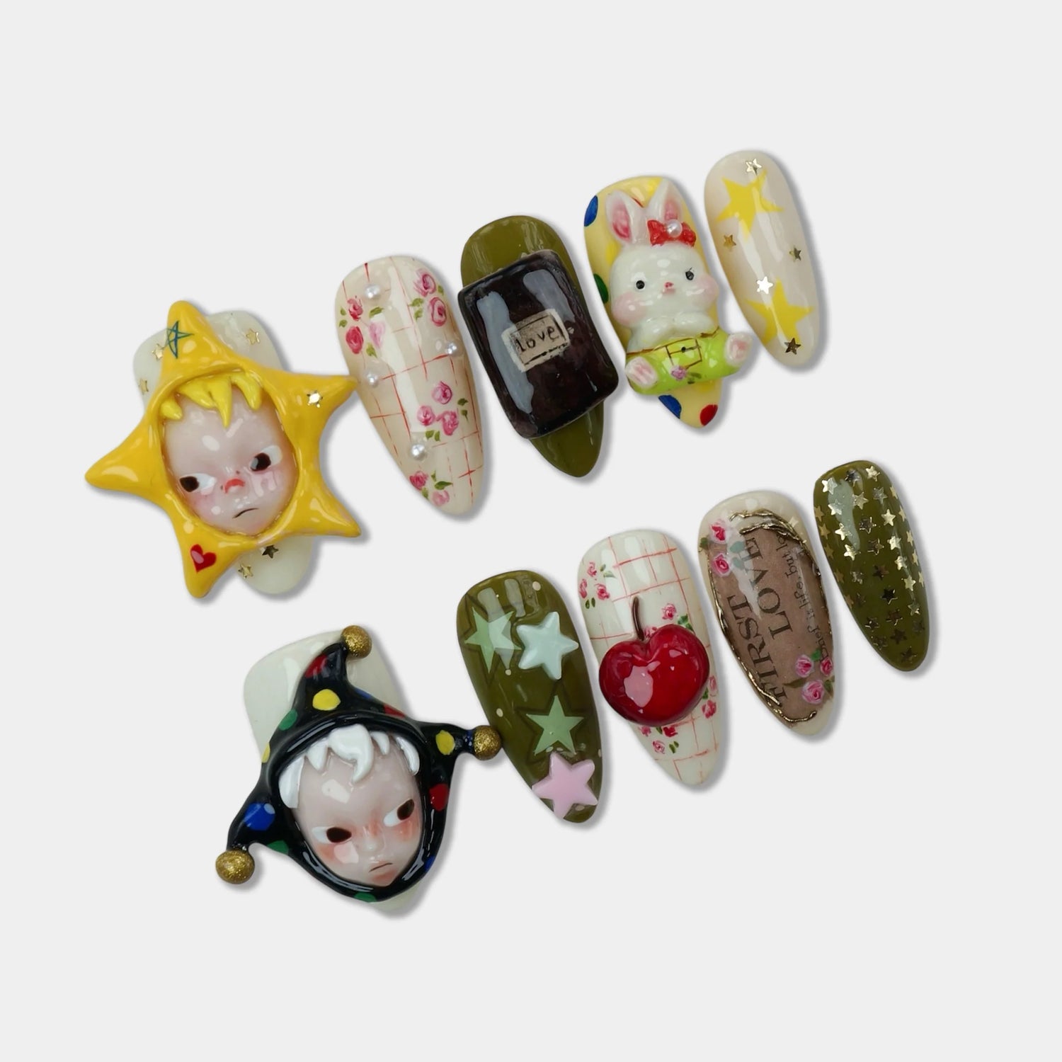 Hirono press-on nail set flat lay featuring two 3D Hirono character face charms in star and jester hat frames, alongside accent nails with rose floral plaid art, love bottle nail, 3D bunny charm, star motifs, cherry charm, and FIRST LOVE script