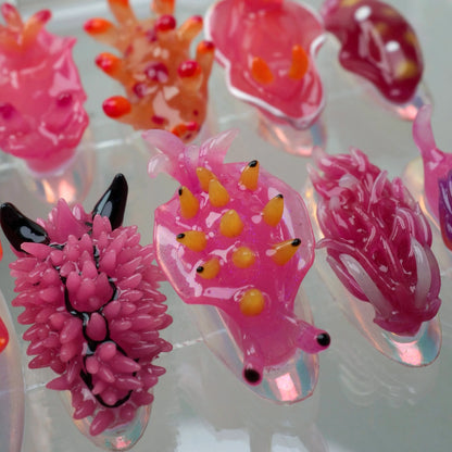 A set of press-on nails designed to resemble colorful nudibranchs (sea slugs), displayed in a clear case. Each nail features a unique sea slug-inspired design with vibrant hues of pink, blue, orange, and purple, and detailed textures imitating the creatures' shapes and appendages