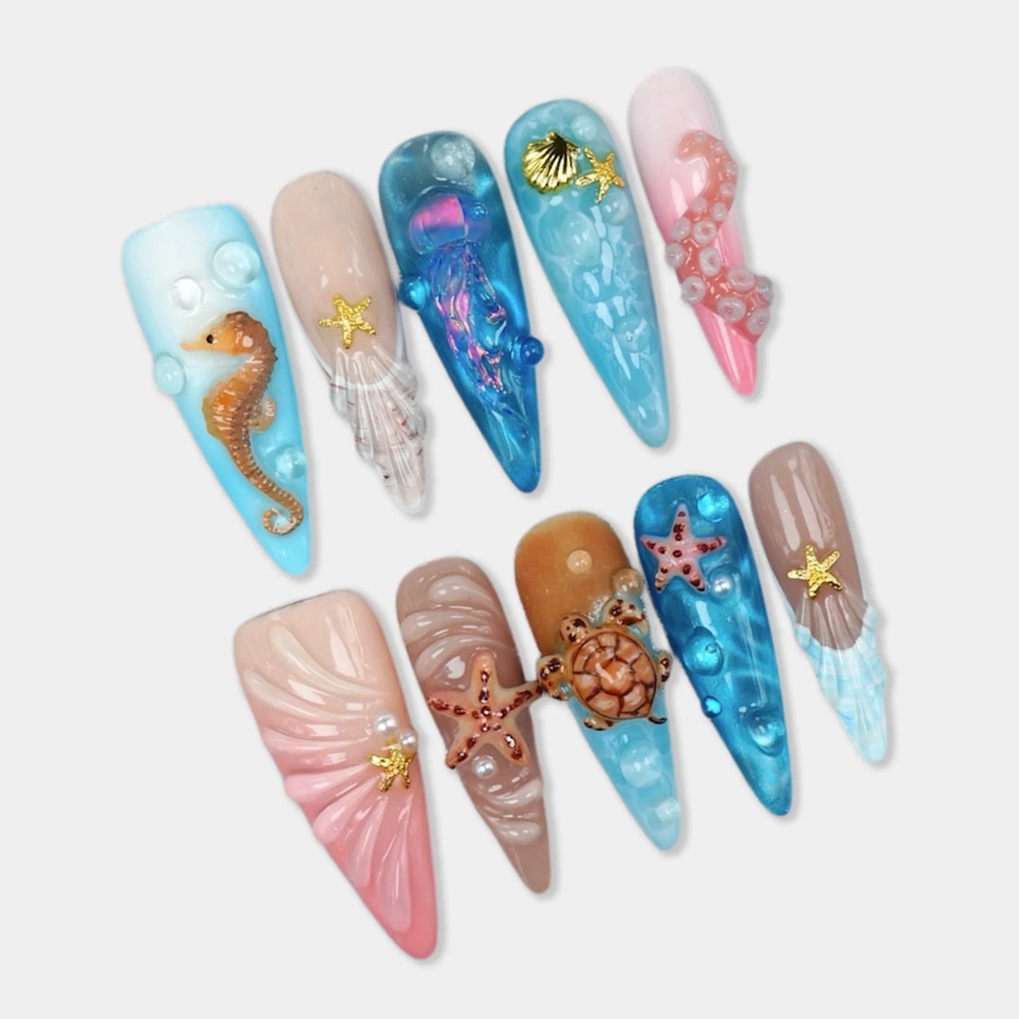 Aquatic press-on nail set, 10 stiletto nails with ocean theme featuring 3D seahorse, sea turtle, iridescent jellyfish, and starfish charms on baby blue, nude, pink, and sandy beige with shell textures and pearl bubble accents