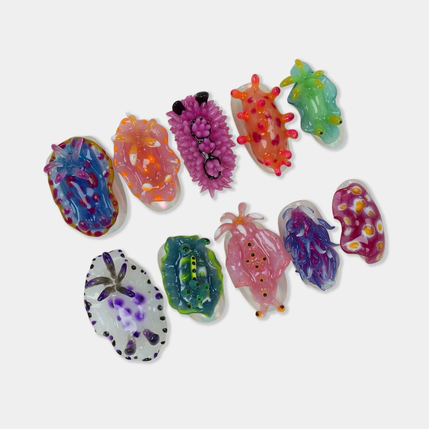 Sea Slug Color press-on nail set flat lay showing 10 oval nails each sculpted as a unique colorful nudibranch including blue-spotted, purple spiky, orange-spiked, pink, teal leaf slug, and white polka-dot sea slug designs