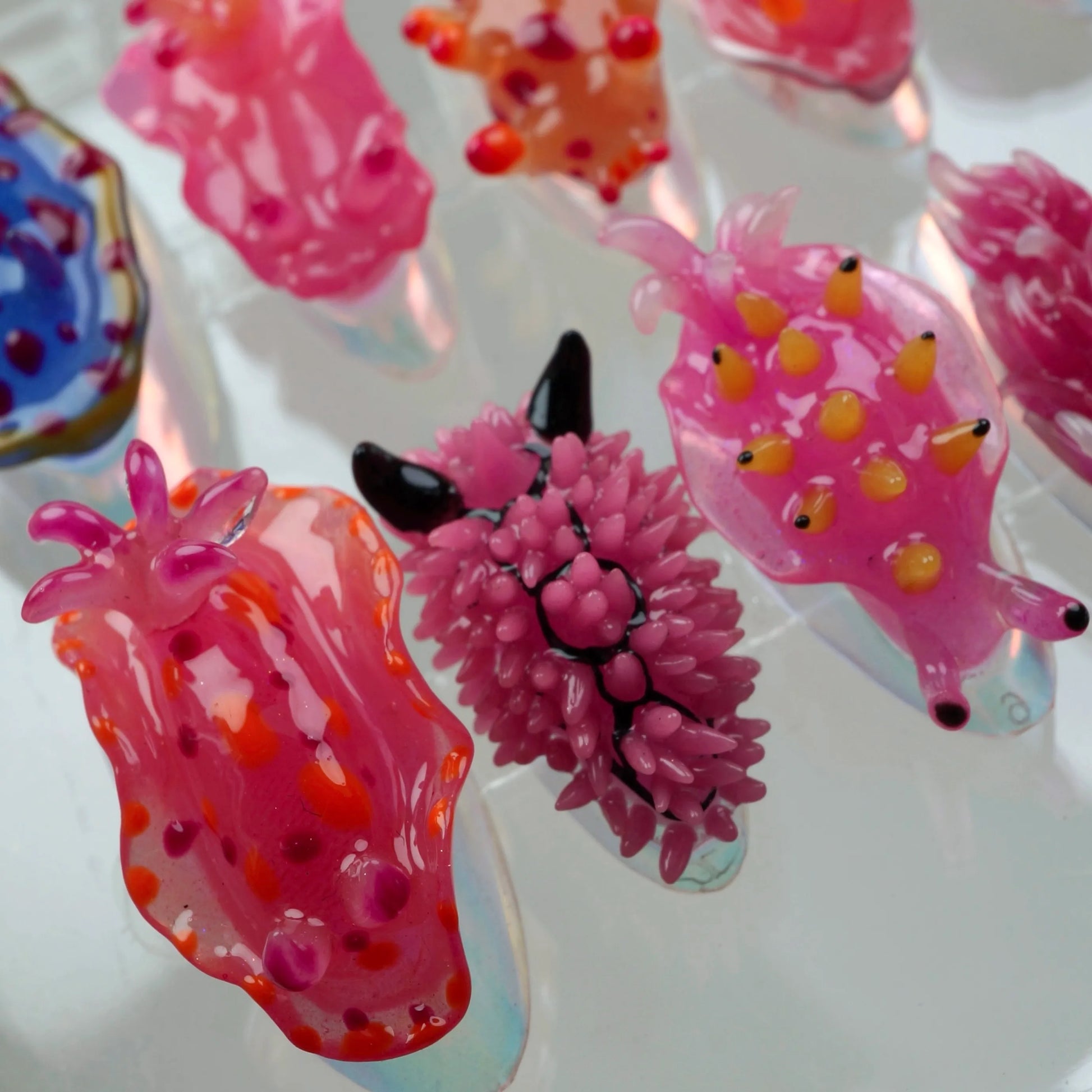 A set of press-on nails designed to resemble colorful nudibranchs (sea slugs), displayed in a clear case. Each nail features a unique sea slug-inspired design with vibrant hues of pink, blue, orange, and purple, and detailed textures imitating the creatures' shapes and appendages