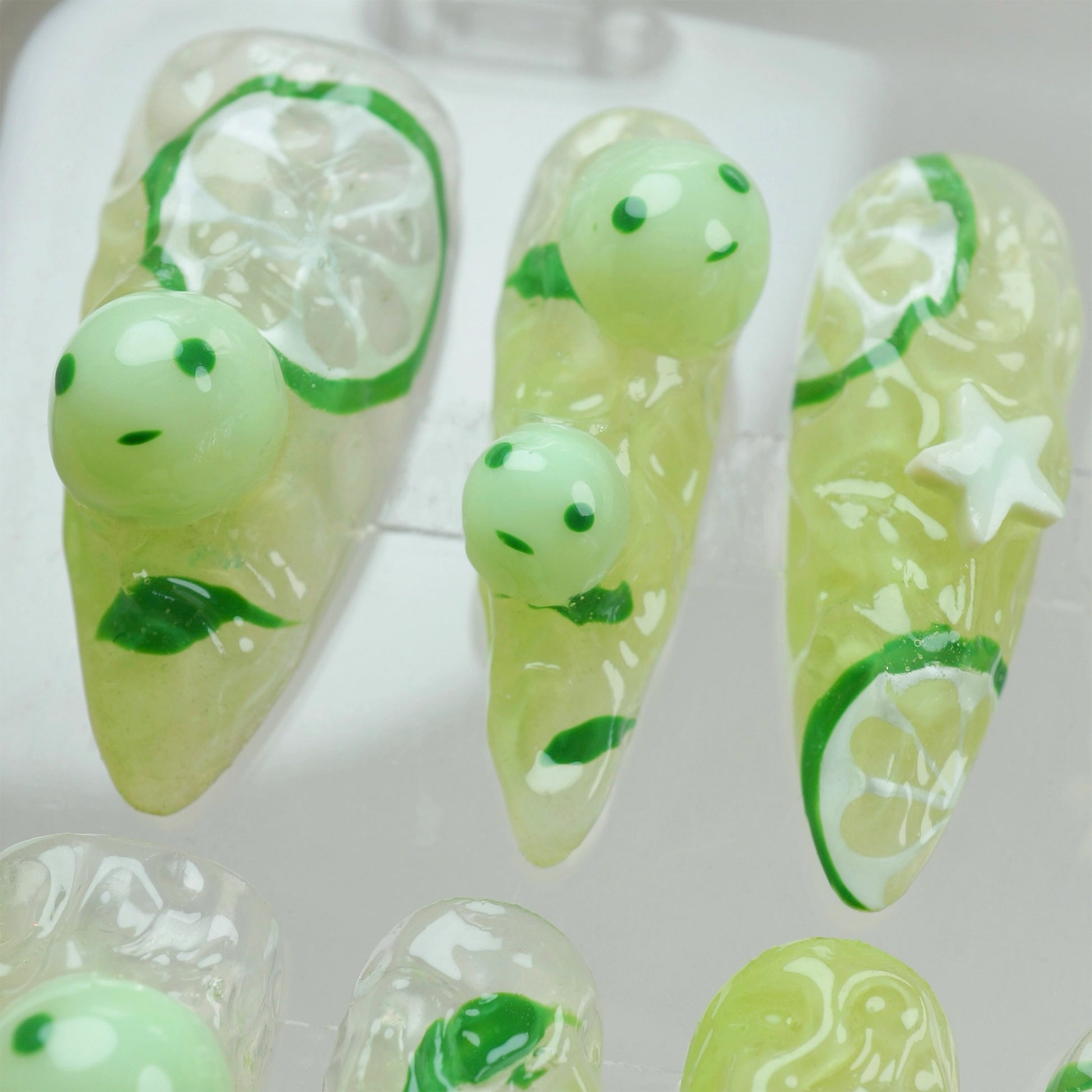 Smiski-inspired press-on nails by Donailsart with lime green tones, citrus slice details, and glowing mini smiski faces for a fun, quirky vibe