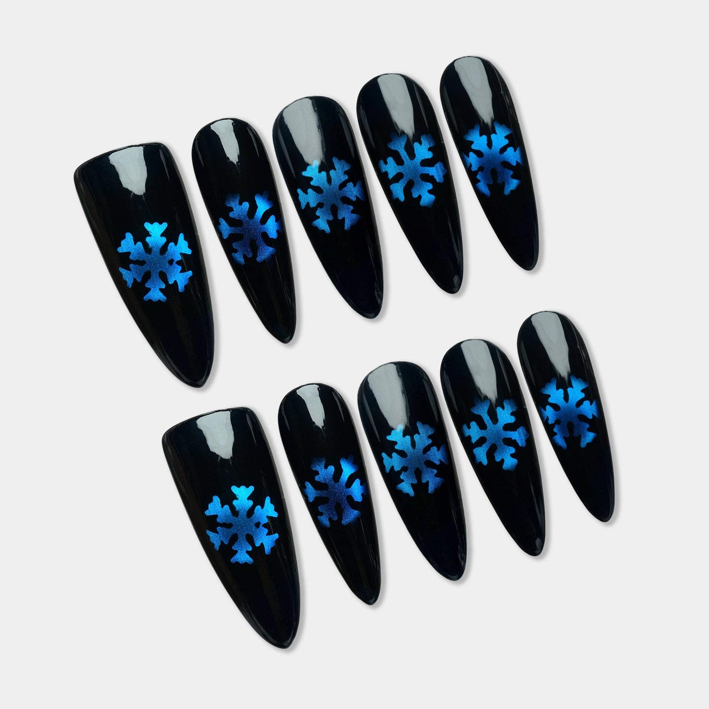 Glossy black press-on nails with metallic blue snowflake designs, inspired by a frosty winter night.