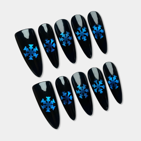 Glossy black press-on nails with metallic blue snowflake designs, inspired by a frosty winter night.